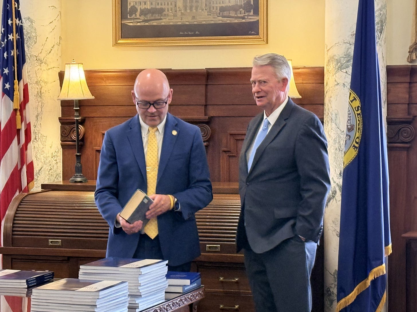 Secretary of State Phil McGrane and Governor Brad Little examine previous editions of the Idaho Blue Book at a media event in May 2026.