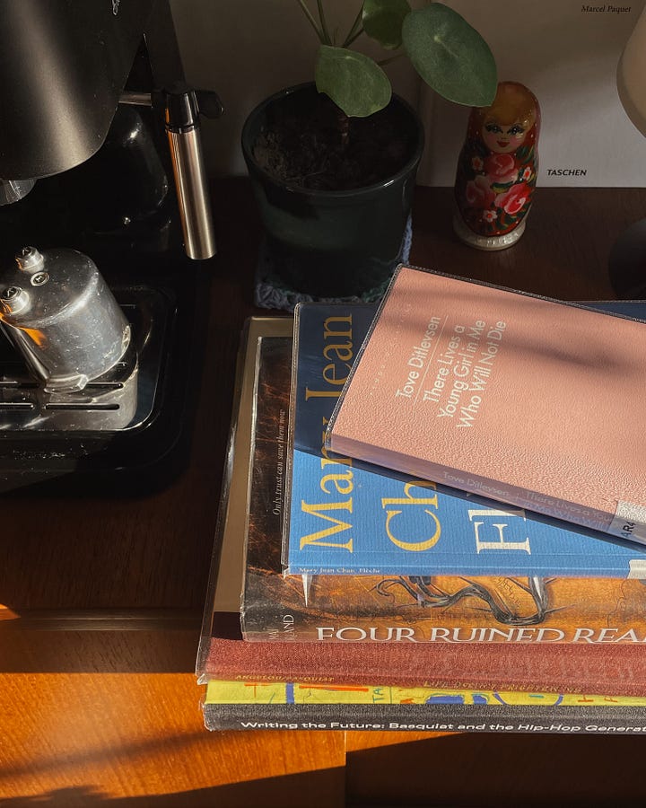 March TBR - Image 1: A stack of library books on my coffee station, with a coffee machine and decor in the background. / Image 2: A close-up of the book stack.