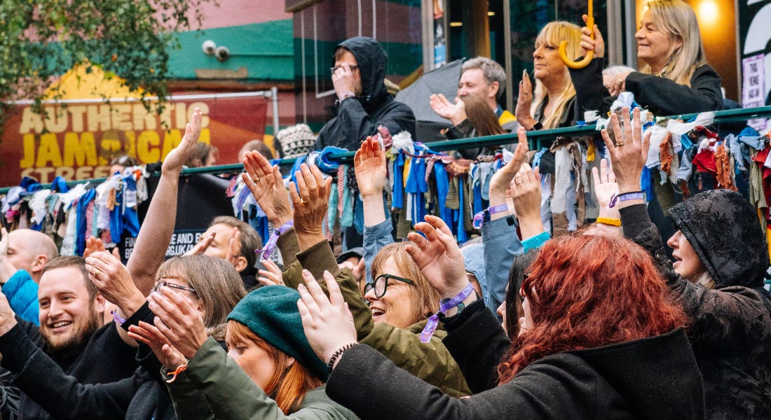A group of people with their hands in the air, with a colourful cinema behind them A group of people with their hands in the air, with a colourful cinema behind them