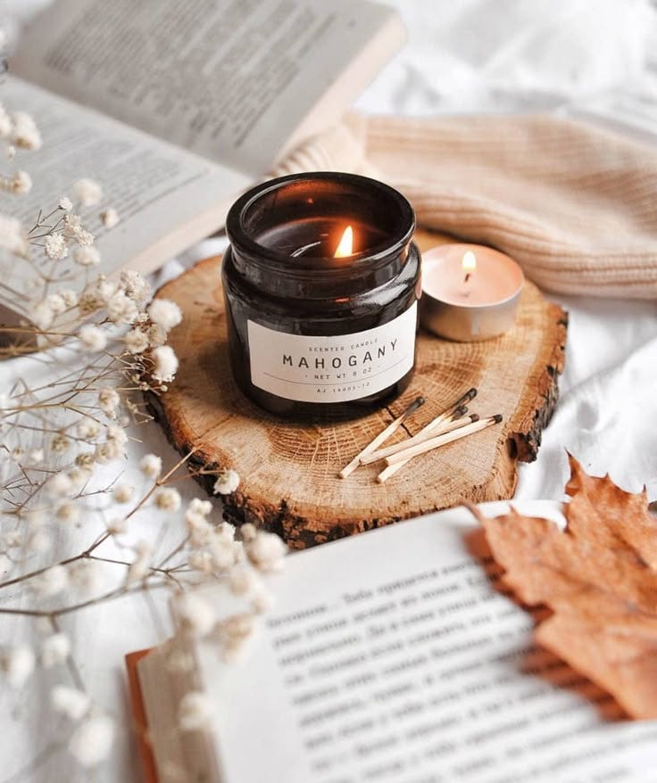 This may contain: an open book and some candles on a wooden slice with leaves next to it in the foreground