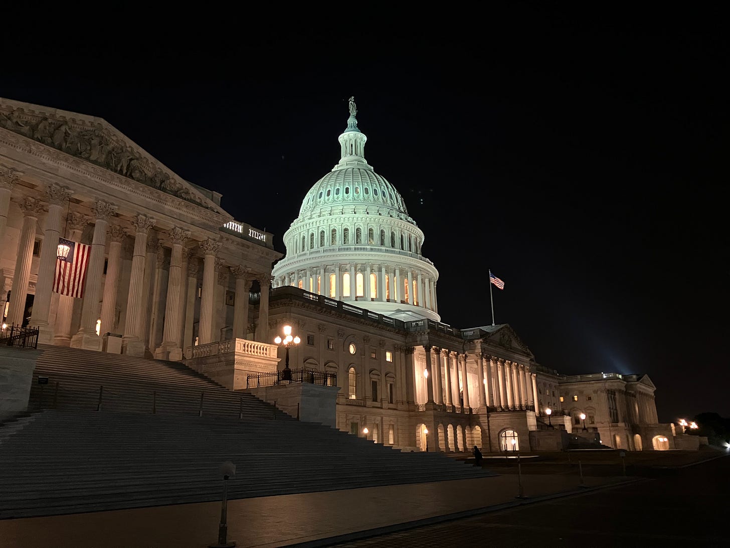 The U.S. Capitol building at night, illuminated against a dark sky. The steps and surrounding plaza are empty, highlighting the quiet and solemn atmosphere.