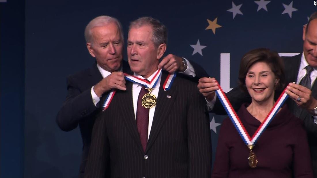 Joe Biden putting a medal around the neck of former President and war criminal George W. Bush