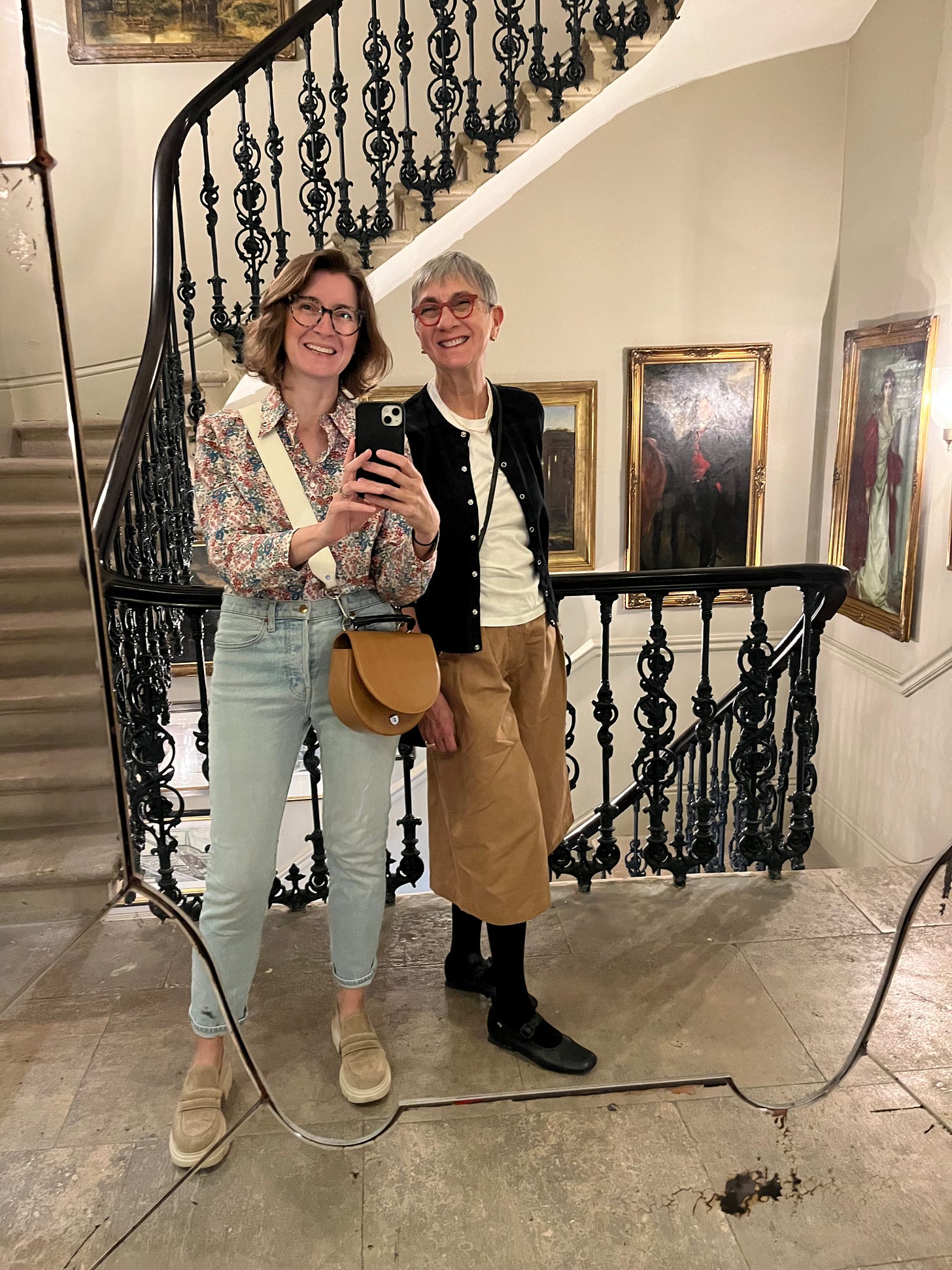 Two women smiling and taking a selfie with stairs behind them.