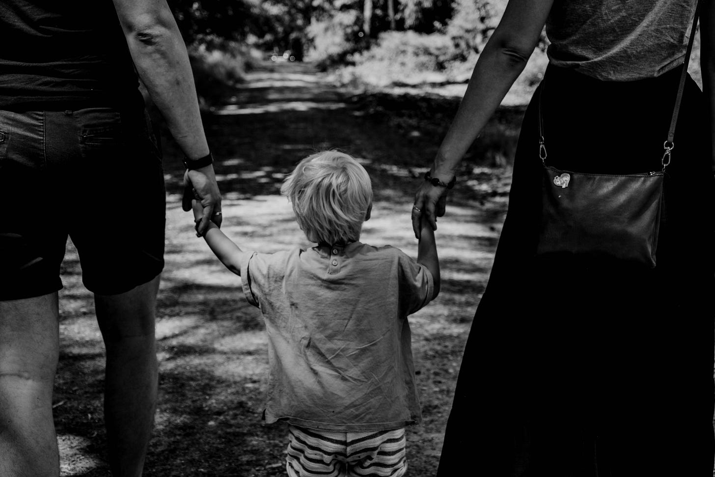 black and white photo of blonde child holding hands with parents black and white photo of blonde child holding hands with parents