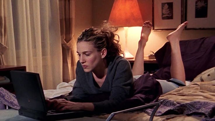 This may contain: a woman laying on her bed with a laptop computer in front of her, while another person lays down next to her
