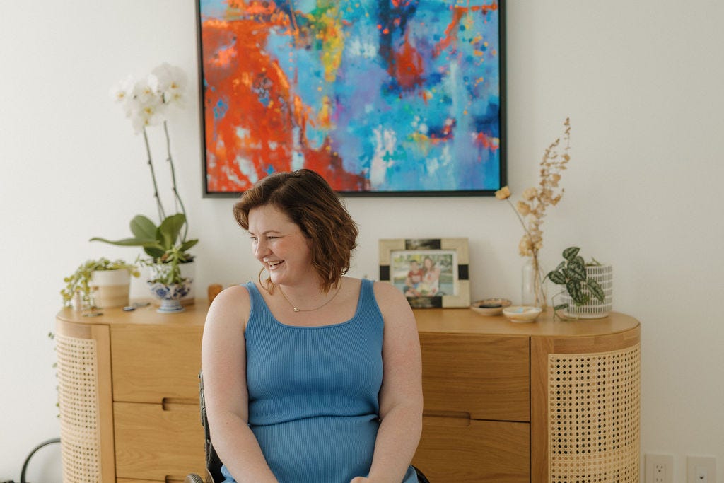 A white woman with short brown hair sitting in front of a painting in her manual wheelchair
