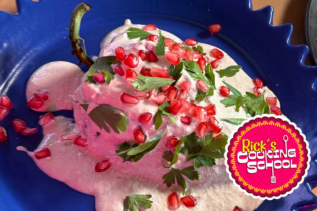 Close up of a chile en nogada with walnut sauce, pomegranate seeds and parsley leaves.
