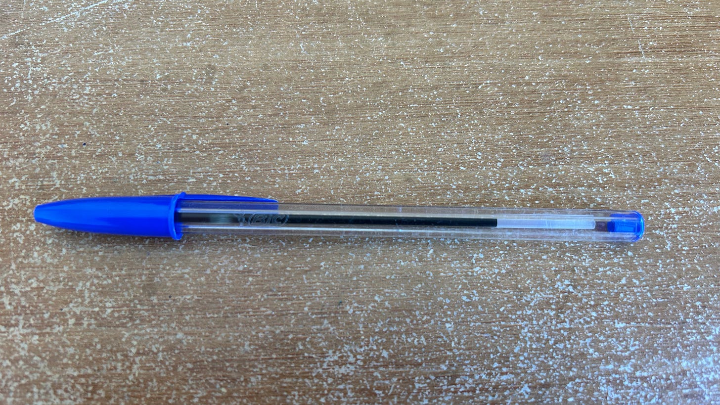 A blue Bic Crystal ballpoint pen. It is lying on a desk. 