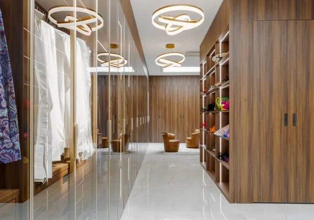 walk in closet with built in cubes for clothes and a hanging closet opposite with clear doors and two small leather chairs in the far background and large circular light fixtures walk in closet with built in cubes for clothes and a hanging closet opposite with clear doors and two small leather chairs in the far background and large circular light fixtures
