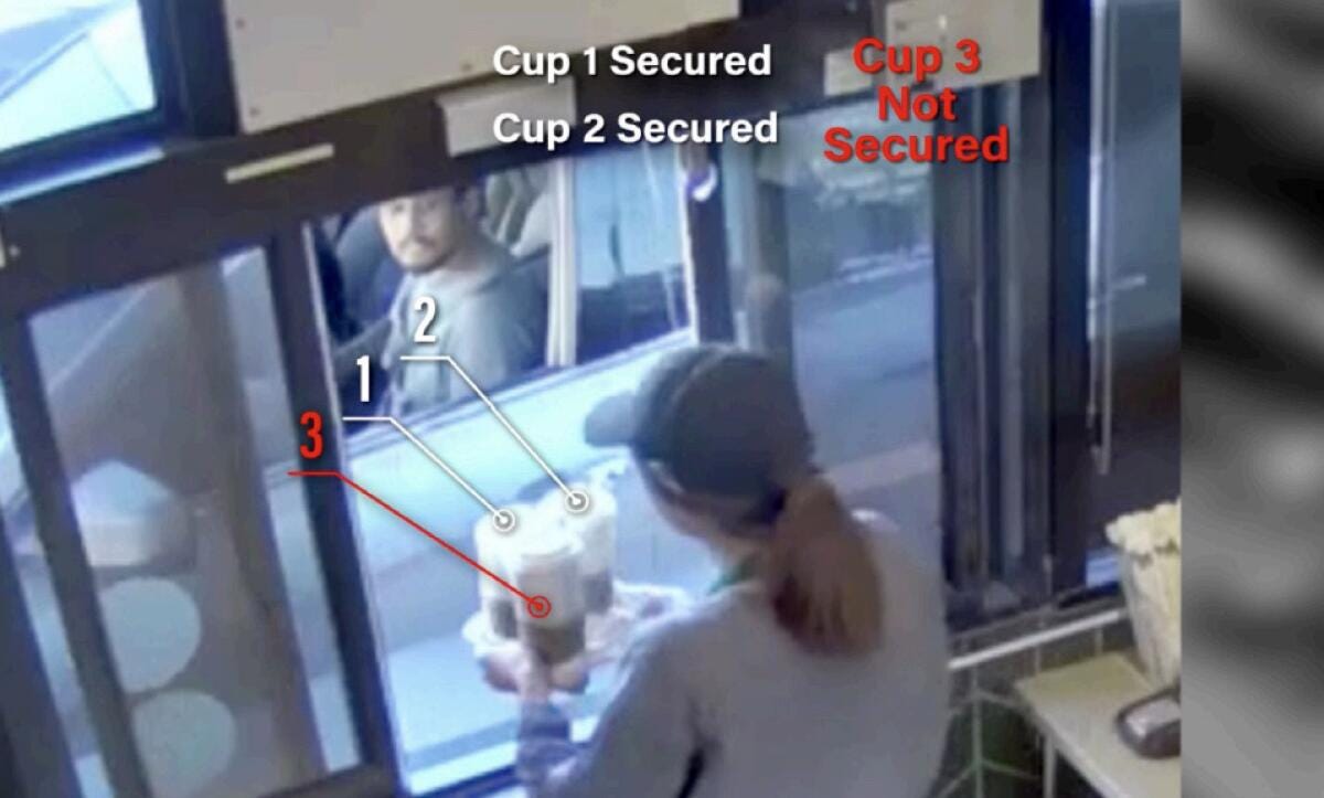 An image from video of an employee handing a tray of drinks through drive-through window
