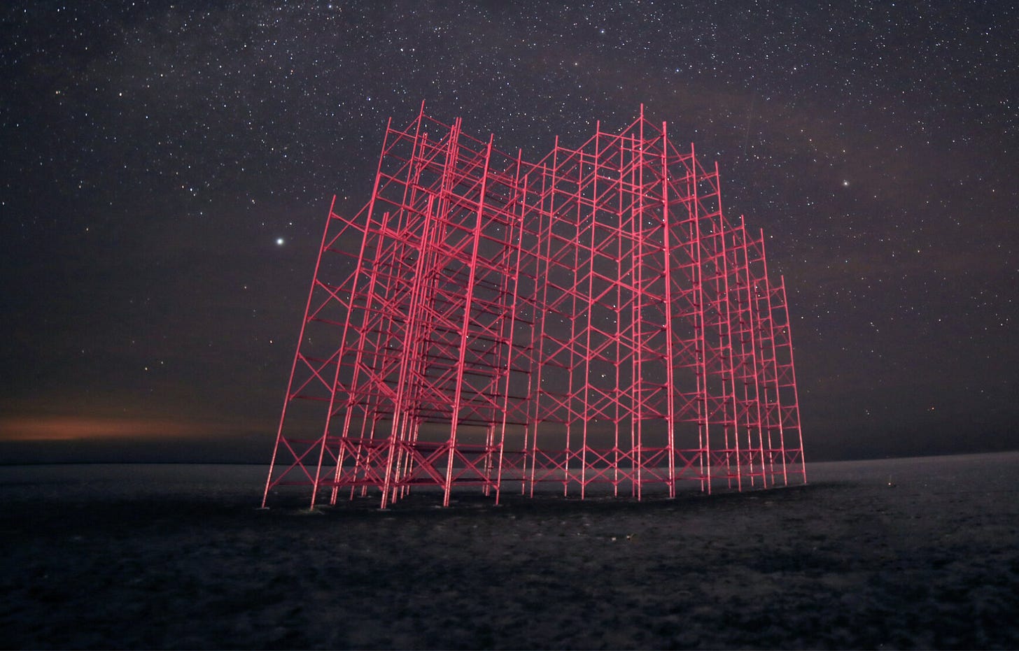 A 40-ft hot pink scaffolding lit up at night with a starry black sky behind it.