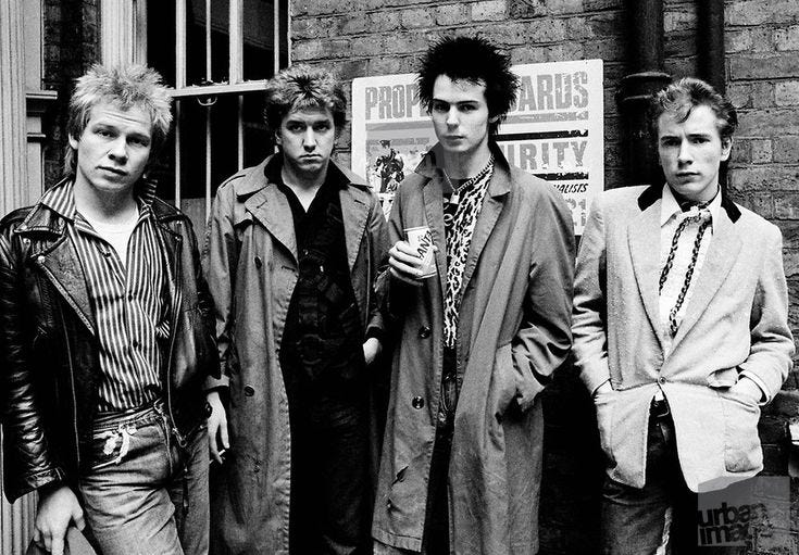 This may contain: black and white photograph of four young men standing in front of a brick building, one holding a drink This may contain: black and white photograph of four young men standing in front of a brick building, one holding a drink
