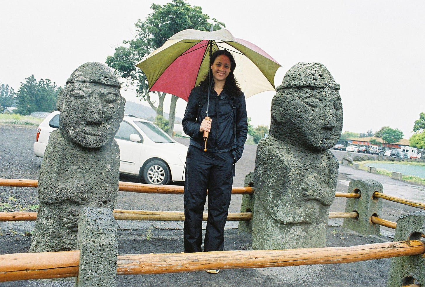 A woman holds an umbrella as she stands between two dol hareubang statues in Jeju Island, South Korea. A woman holds an umbrella as she stands between two dol hareubang statues in Jeju Island, South Korea.