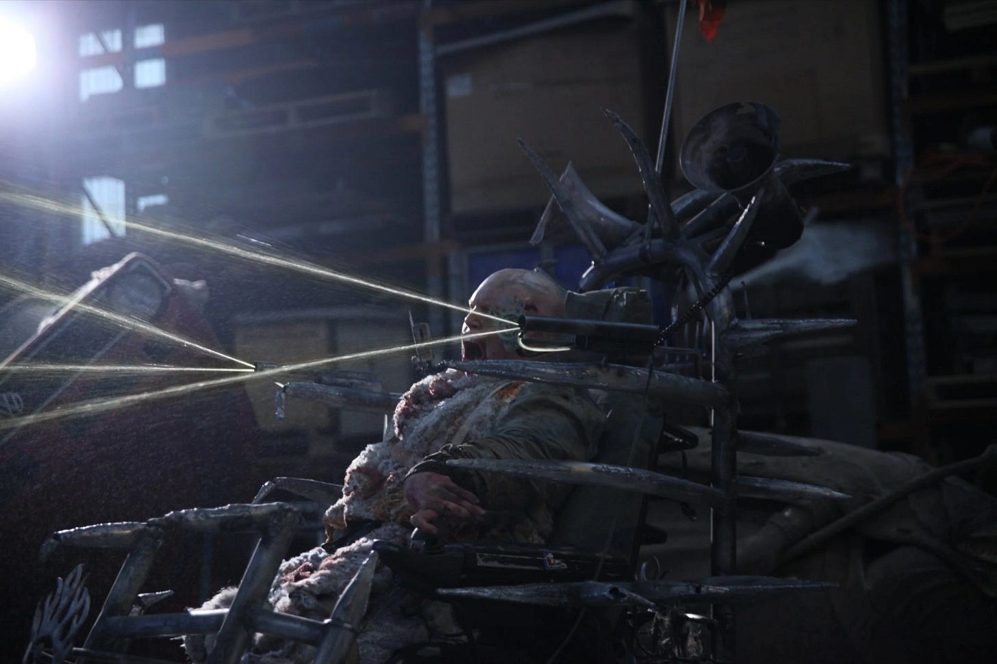 A dirty and bleeding white disabled person is in an wheelchair made of heavy metal. It’s giving Mad Max vibes. 5 streams of piss are shooting out from the front of the chair.