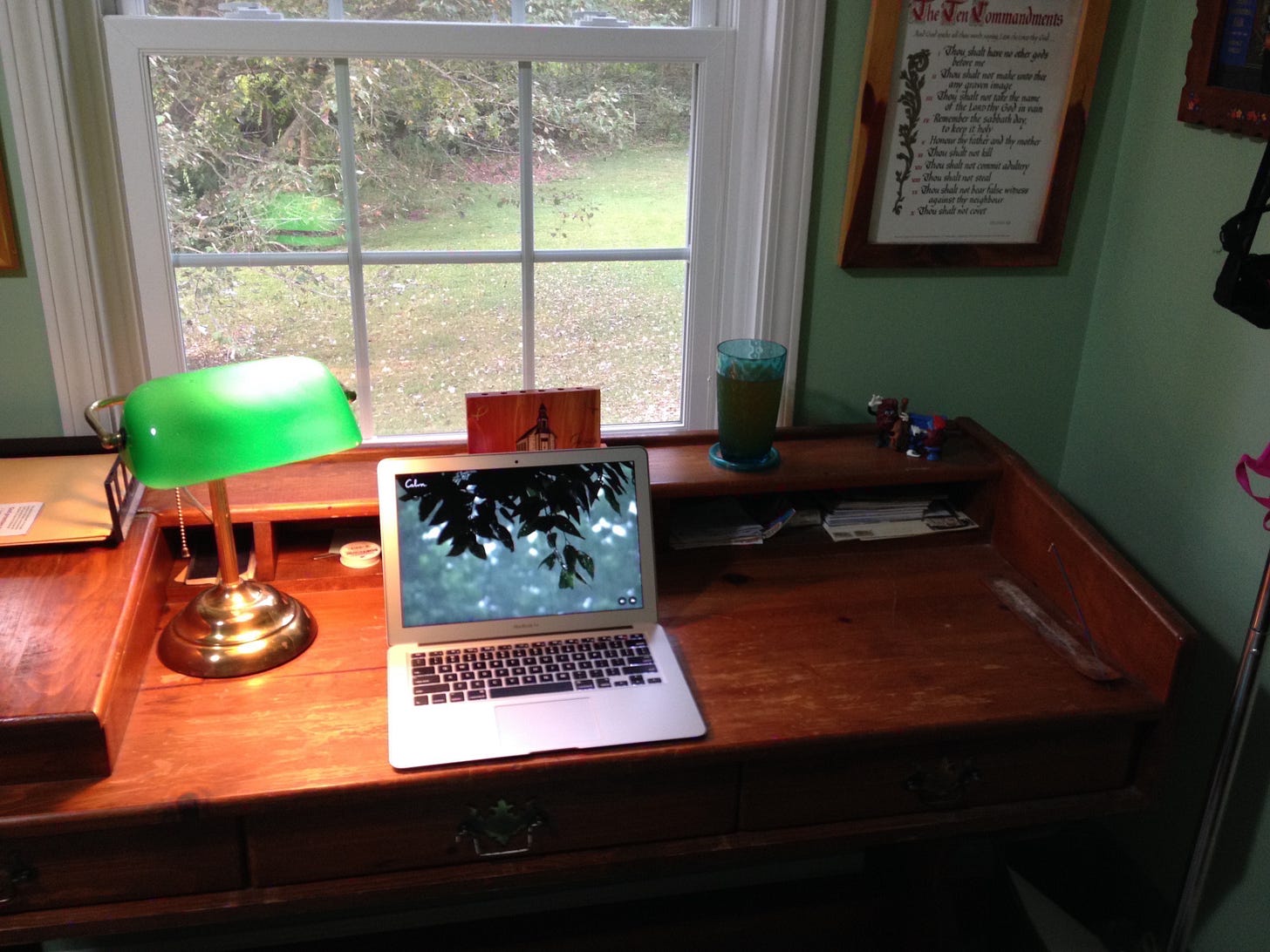 Macbook air laptop on a handmade wooden desk with a green lamp overlooking a window outdoors