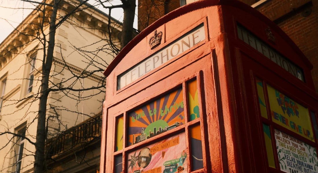 A red phone box with artwork on it with a white building behind it A red phone box with artwork on it with a white building behind it