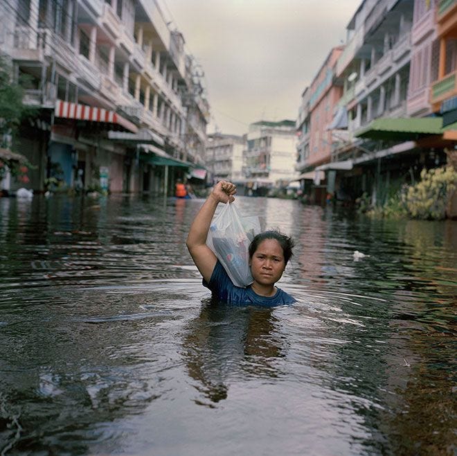 This may contain: a woman is wading through the water in a flooded area with buildings on either side