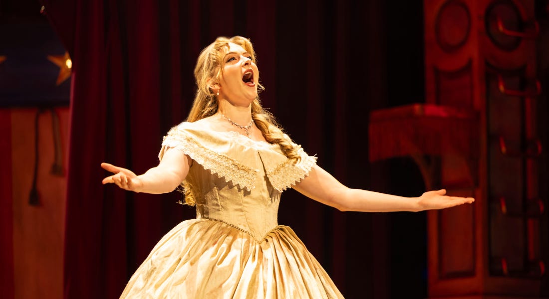 A woman wearing a white dress and blonde wig singing, with a red backdrop in the background A woman wearing a white dress and blonde wig singing, with a red backdrop in the background