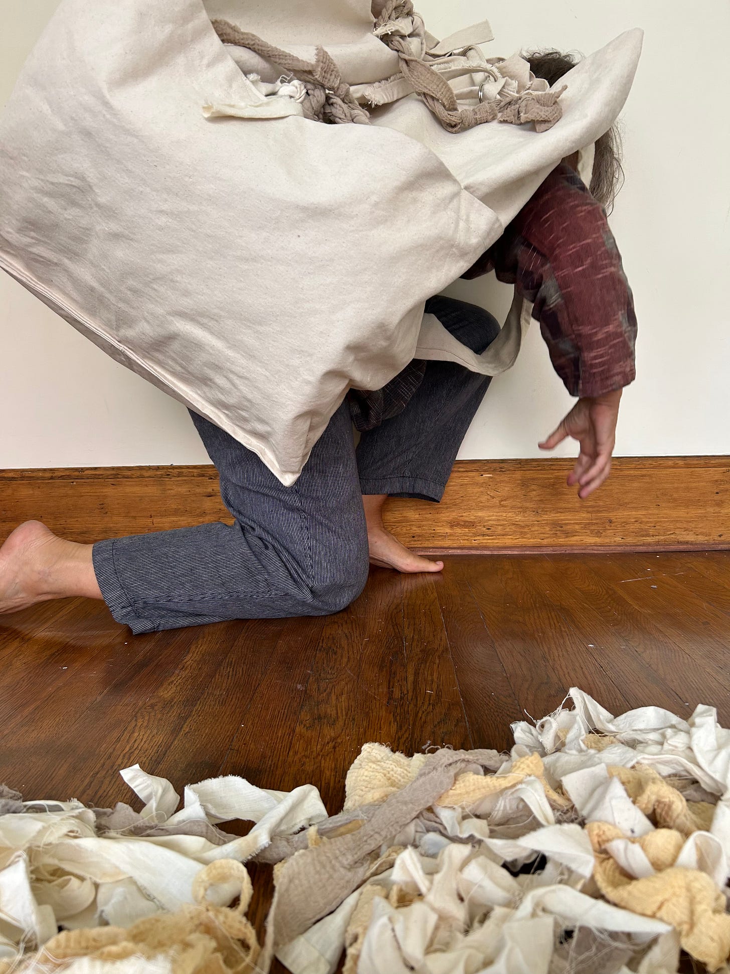 a person is bent over, almost kneeling, carrying a very large canvas bag over their shoulders, concealing the top half of their body.