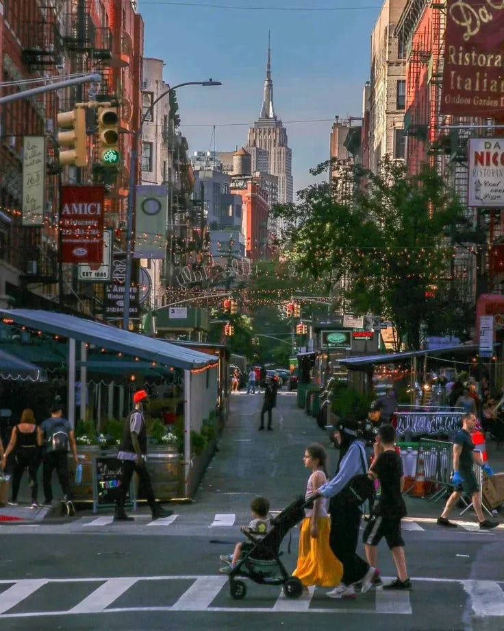 This may contain: people are crossing the street at an intersection in new york city, with tall buildings behind them This may contain: people are crossing the street at an intersection in new york city, with tall buildings behind them
