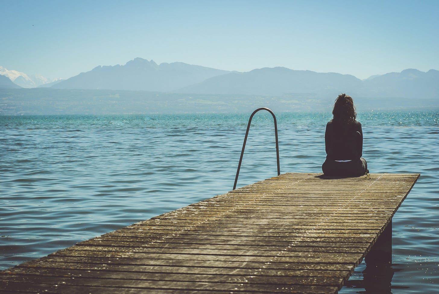 Woman sitting on dock looking at lake and mountains Woman sitting on dock looking at lake and mountains