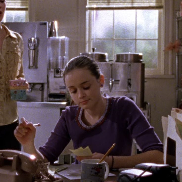 This may contain: two women sitting at a table in a kitchen, one writing on a piece of paper