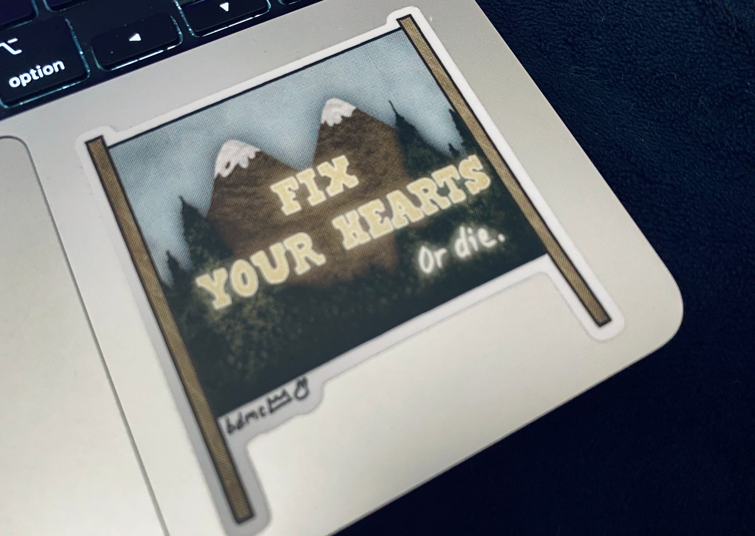 Sticker on a laptop shaped like the Welcome to Twin Peaks sign, reading instead “Fix Your Hearts or Die.” Sticker on a laptop shaped like the Welcome to Twin Peaks sign, reading instead “Fix Your Hearts or Die.”