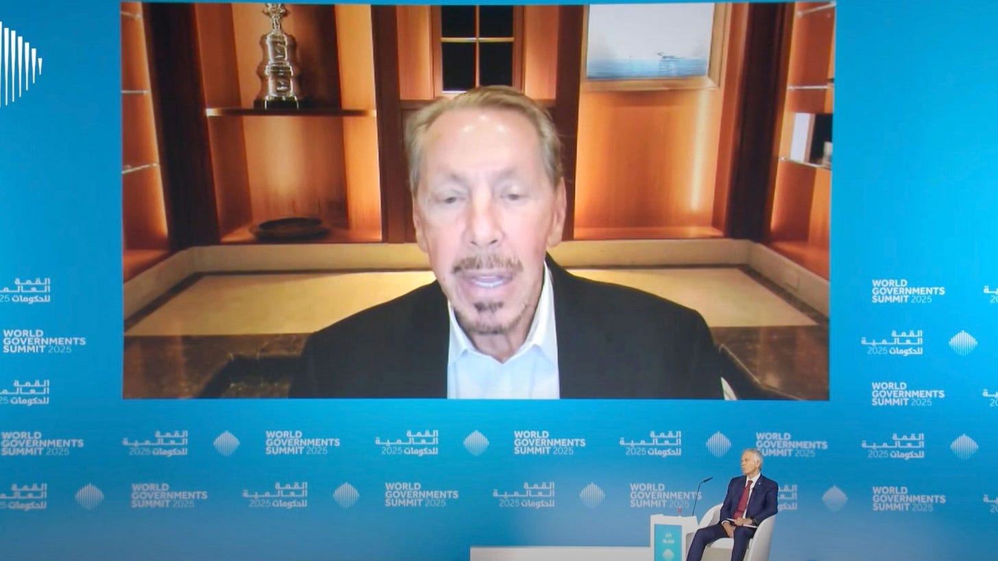 A large screen showing Larry Ellison speaking at the World Government Summit 2025, with a seated Tony Blair in the foreground. A large screen showing Larry Ellison speaking at the World Government Summit 2025, with a seated Tony Blair in the foreground.