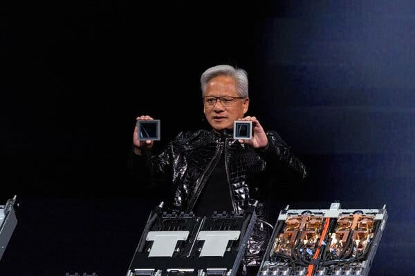 Standing behind computer equipment, Jensen Huang holds up a small square in each hand. 