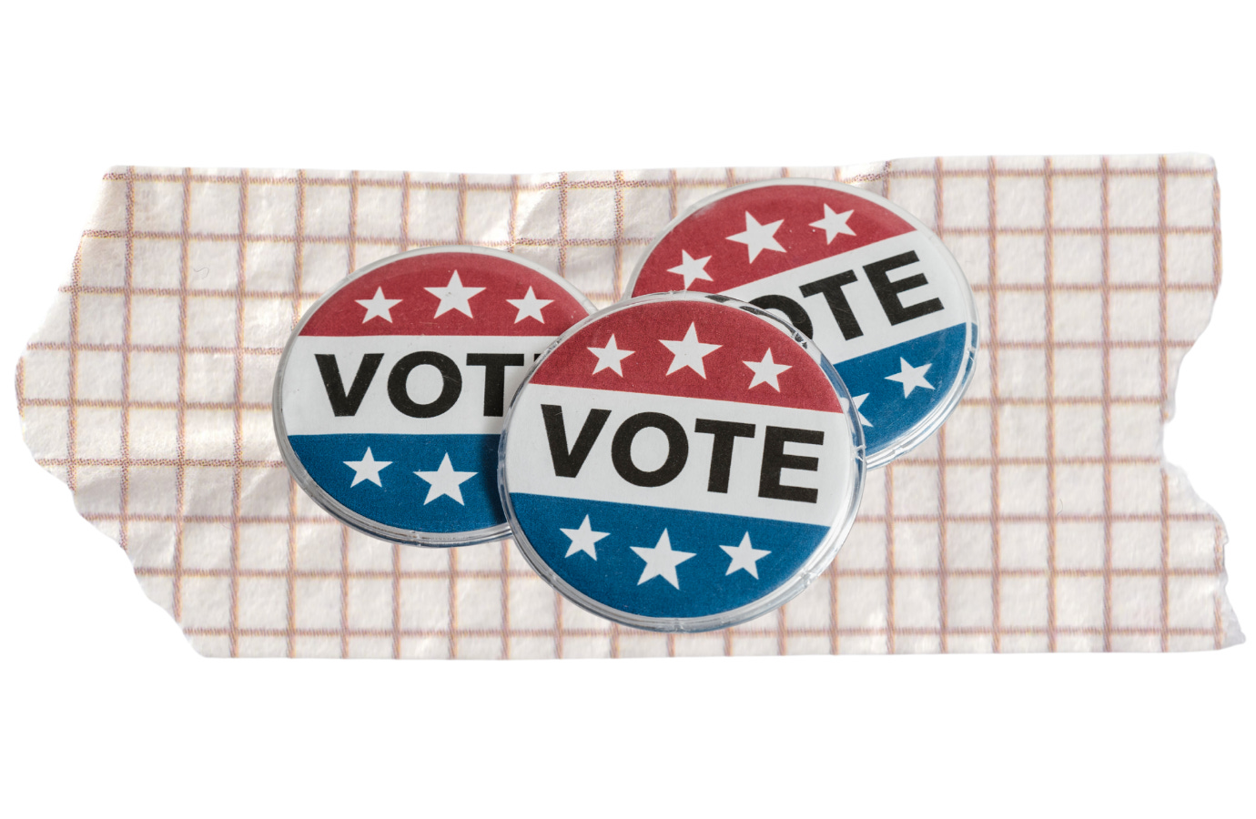 Three red, white, and blue campaign buttons with the word “VOTE” displayed across them, arranged on a piece of patterned tape — symbolizing civic engagement, elections, and voter participation in the United States.
