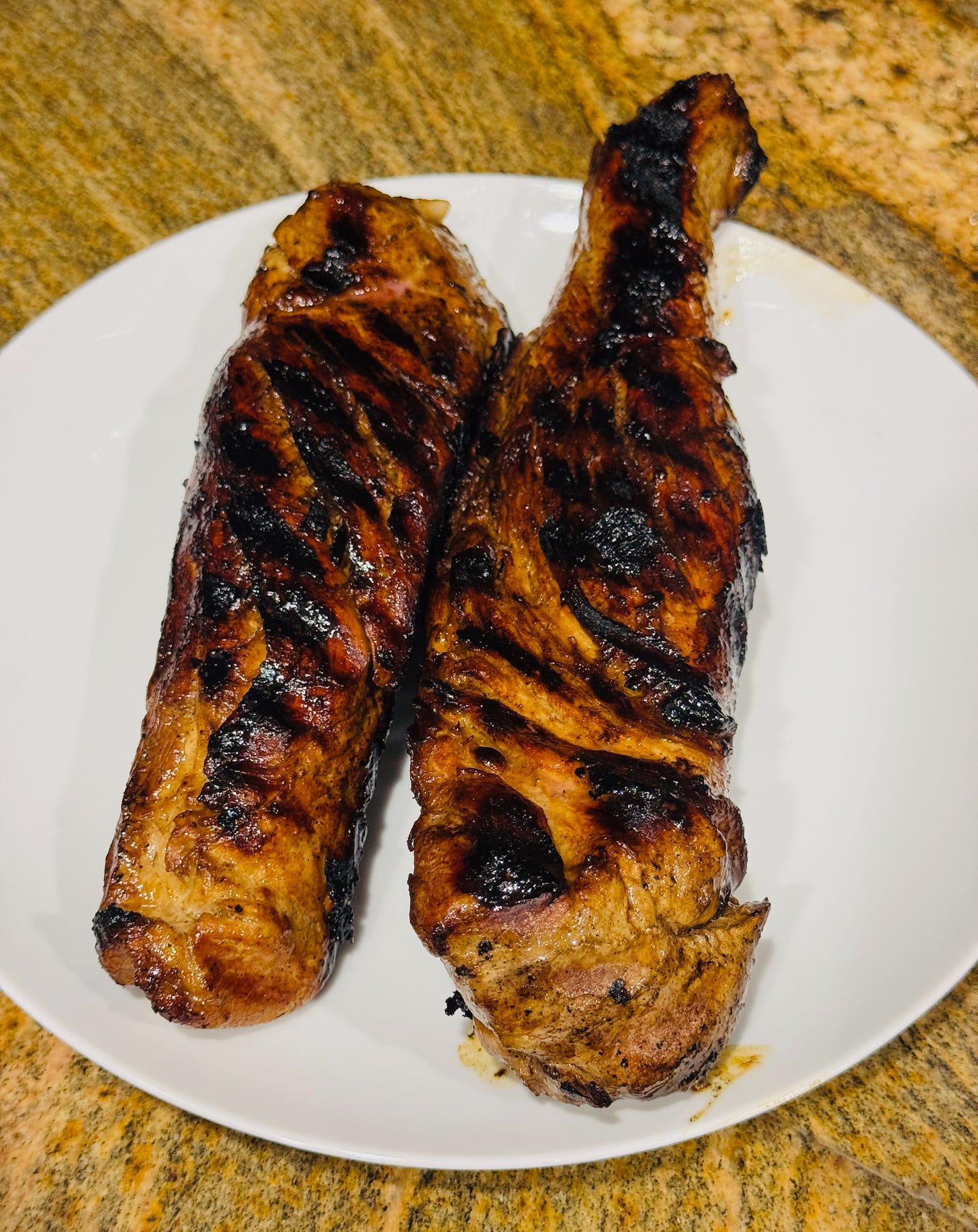Two grilled pork tenderloins charred and caramelized in a grill pan. Two grilled pork tenderloins charred and caramelized in a grill pan.