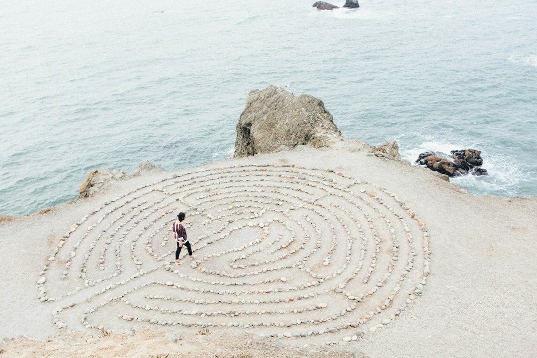 A person walks through a beachfront maze made of white rocks.