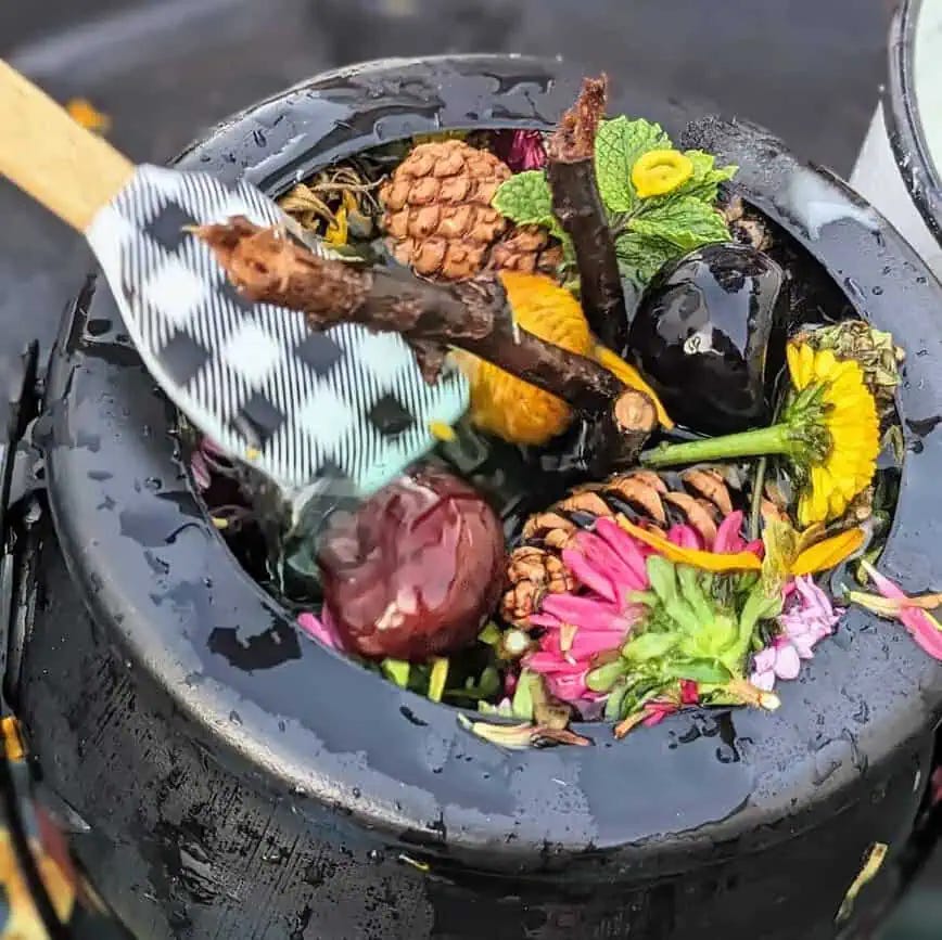 a close up image of a black cauldron which contains conkers, flowers and twigs