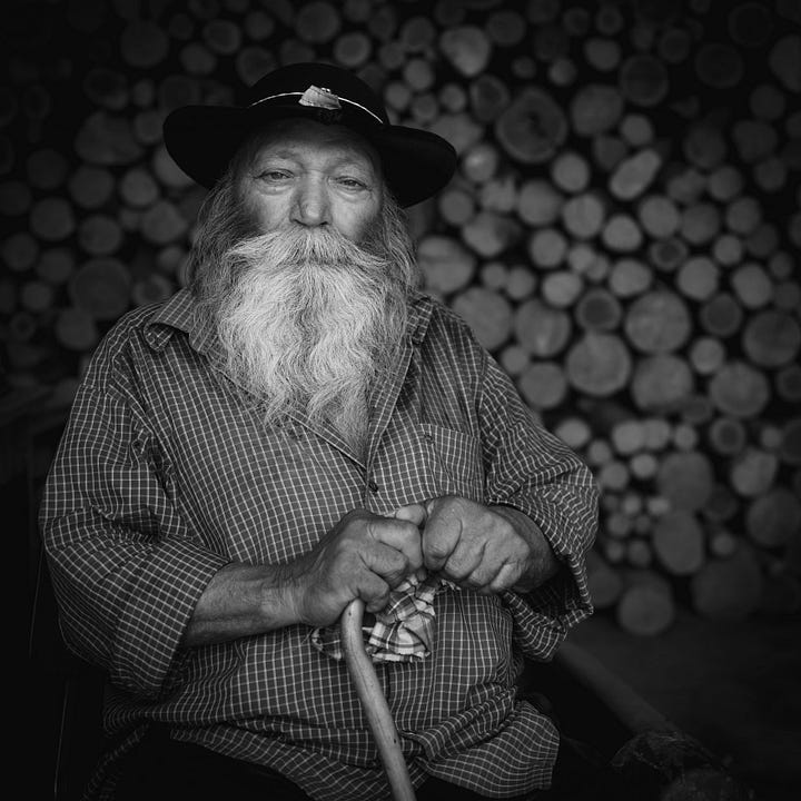 A selection of four images from Romania in black and white, one shows the rural landscape shrouded in mist, the second shows a haystack on a hillside and the other two show a blacksmith and an old man with a magnificent beard 