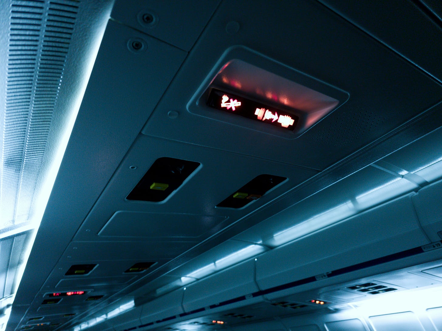 A photo of the ceiling of an airplane with a red illuminated seatbelt sign. A photo of the ceiling of an airplane with a red illuminated seatbelt sign.