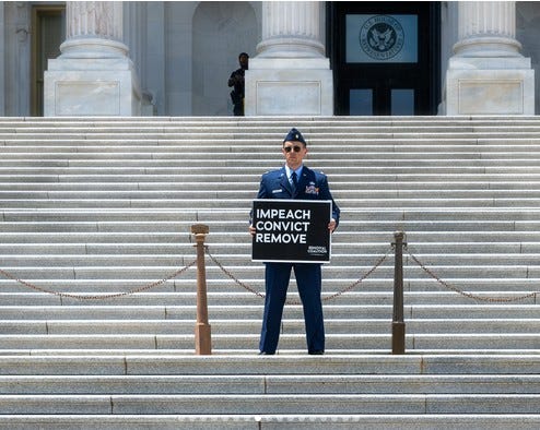 El mayor de la USAF Jason Watson, en las escaleras del Capitolio en Washington, D.C., el 1 de julio, sosteniendo una pancarta que decía: « Enjuiciar políticamente, condenar, destituir» [al presidente]