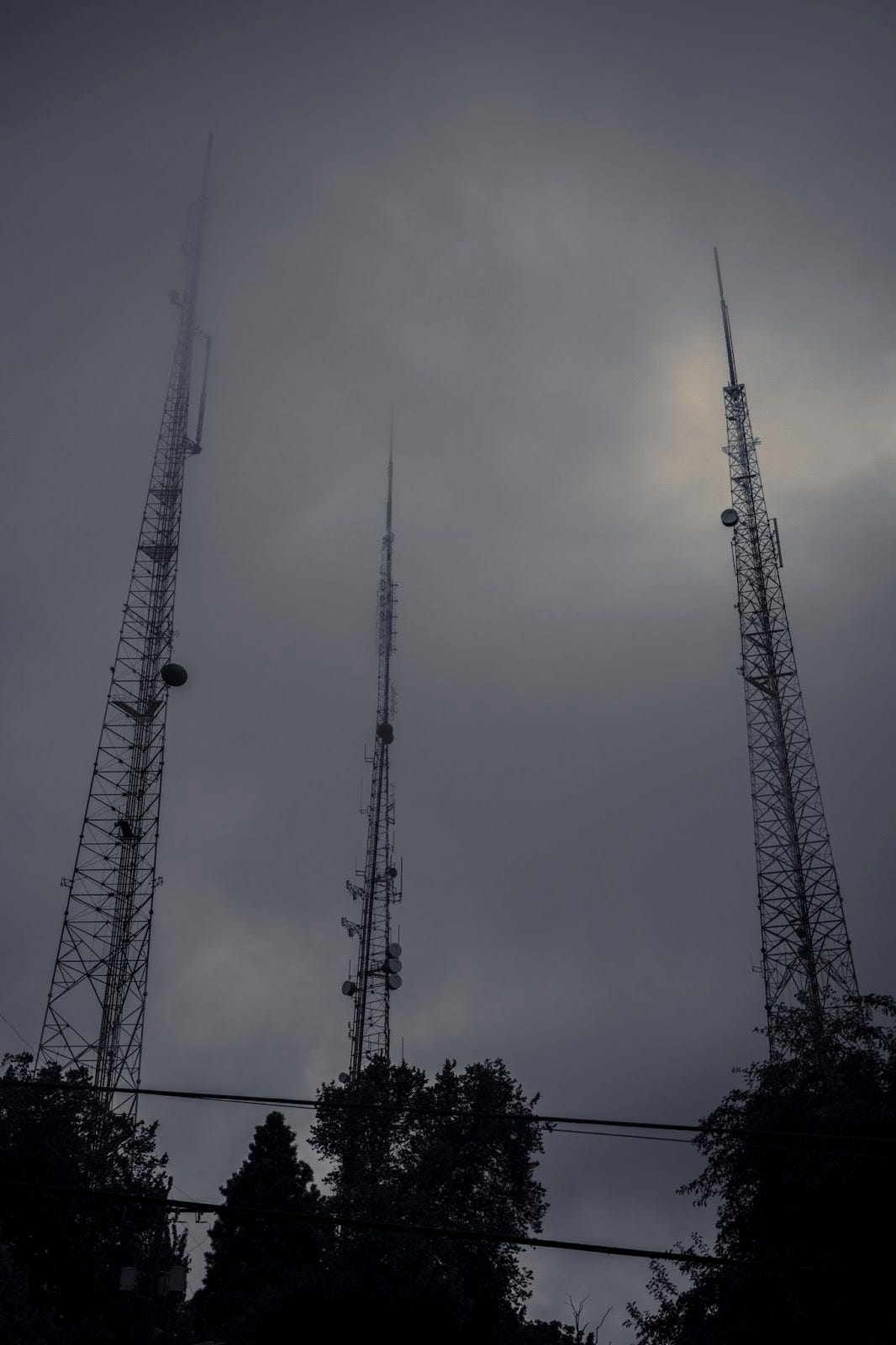 Three enormous cell towers ascend to the point where their tips are obscured by low-hanging clouds.