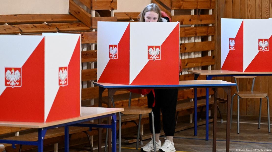 Ein Wahllokal mit drei weiß-roten Wahlkabinen, auf die der polnische Adler aufgedruckt ist. In einer Kabine steht eine junge Frau