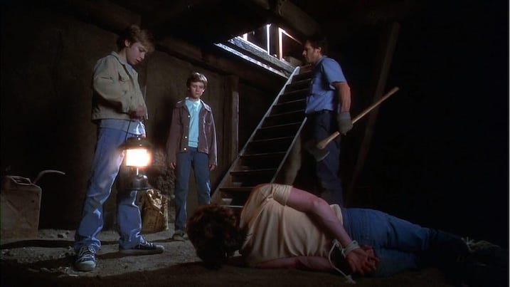 Scene from Frailty showing a father and his two sons standing over a bound man in a dimly lit basement, illuminated by a single lantern.