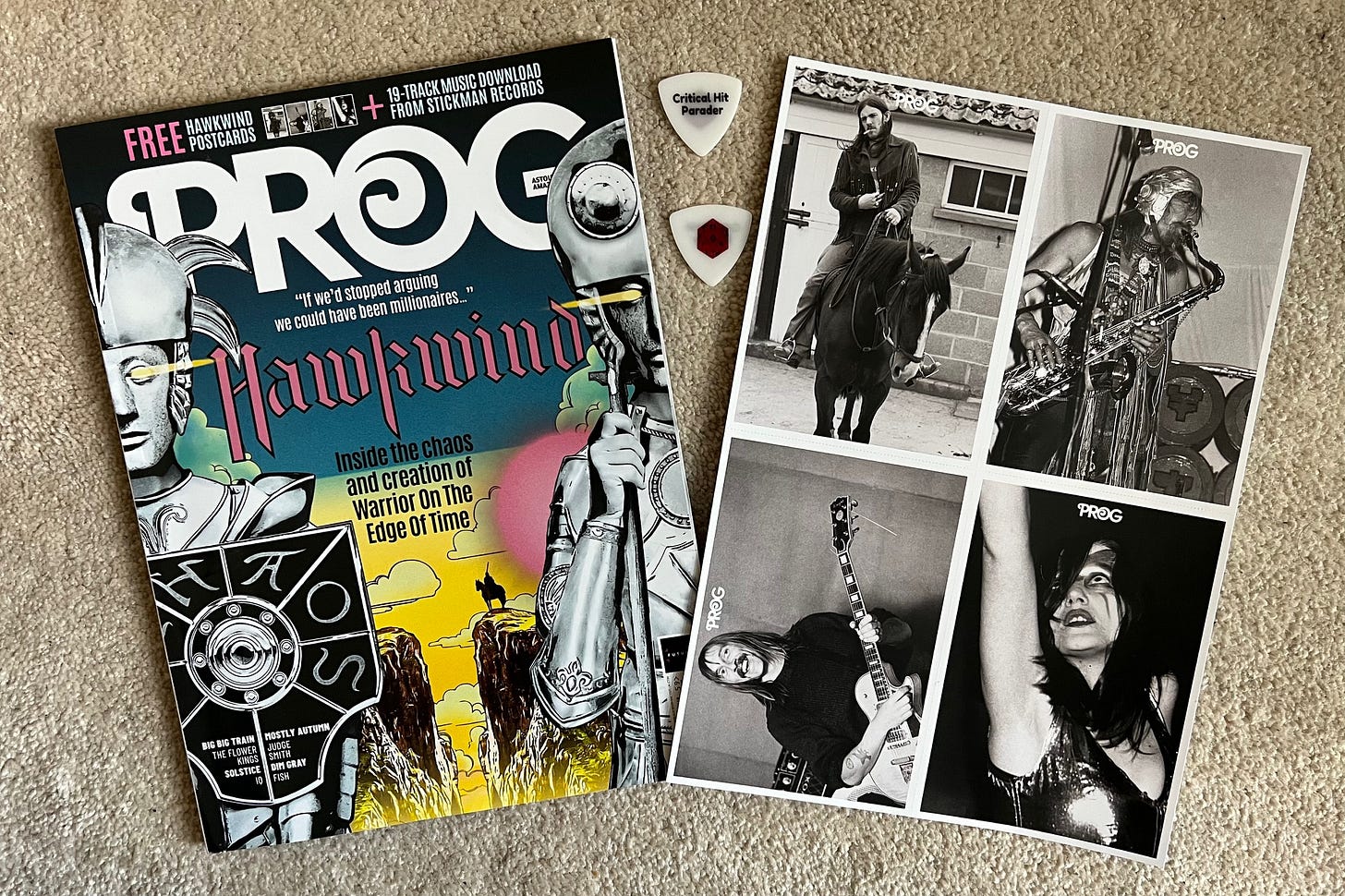 A copy of Prog magazine with band logo for Hawkwind on the cover along with art excerpts from their album Warrior on the Edge of Time (a rider on a horse at the edge of a cliff). Next to the magazine are 4 postcards featuring members of the Hawkwind band (Lemmy on a horse, Dave Brock playing guitar, Nik Turner playing sax, and Stacia cosmically dancing). Between the magazine and the postcards are two white Critical Hit Parader guitar picks enjoying being sandwiched between awesomeness.