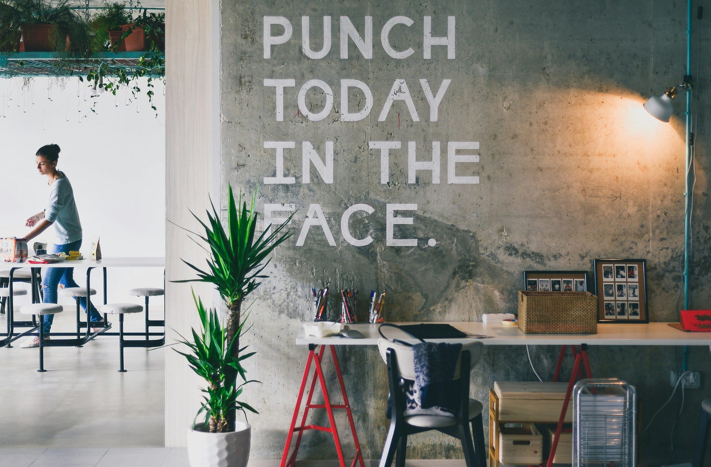 “Punch today in the Face” in plain letters on a grey wall in an artist’s workspace “Punch today in the Face” in plain letters on a grey wall in an artist’s workspace