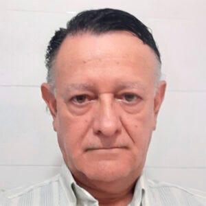 Imagem centralizada do rosto de um homem branco de cabelos escuros com fios grisalhos vestido com uma camisa social branca com listras azuis Imagem centralizada do rosto de um homem branco de cabelos escuros com fios grisalhos vestido com uma camisa social branca com listras azuis
