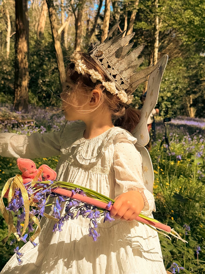 Boy in wizard costume bowing deeply beside girl in fairy costume holding wildflowers in a bluebell forest