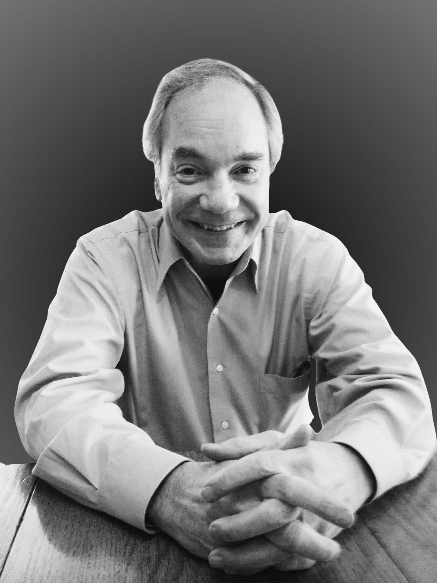 Black and white portrait photograph of legendary coin magician David Roth, smiling at the camera while seated at a table with his hands folded, wearing a collared shirt. Black and white portrait photograph of legendary coin magician David Roth, smiling at the camera while seated at a table with his hands folded, wearing a collared shirt.