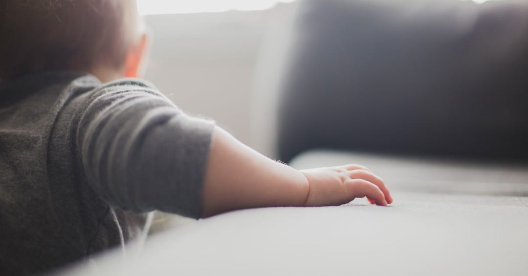 toddler wearing gray shirt holding on to sofa