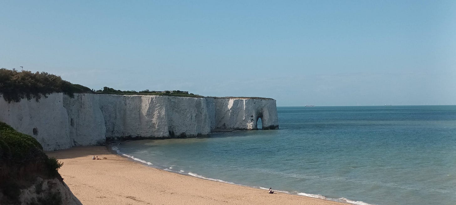 A small bay with tall chalk cliffs in the distance and arches and stacks forming in the chalk geology