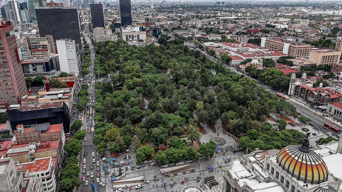 Aerial view of a large tree-filled park in central Mexico City, framed by streets and tall buildings, with a colorful dome in one corner. Aerial view of a large tree-filled park in central Mexico City, framed by streets and tall buildings, with a colorful dome in one corner.