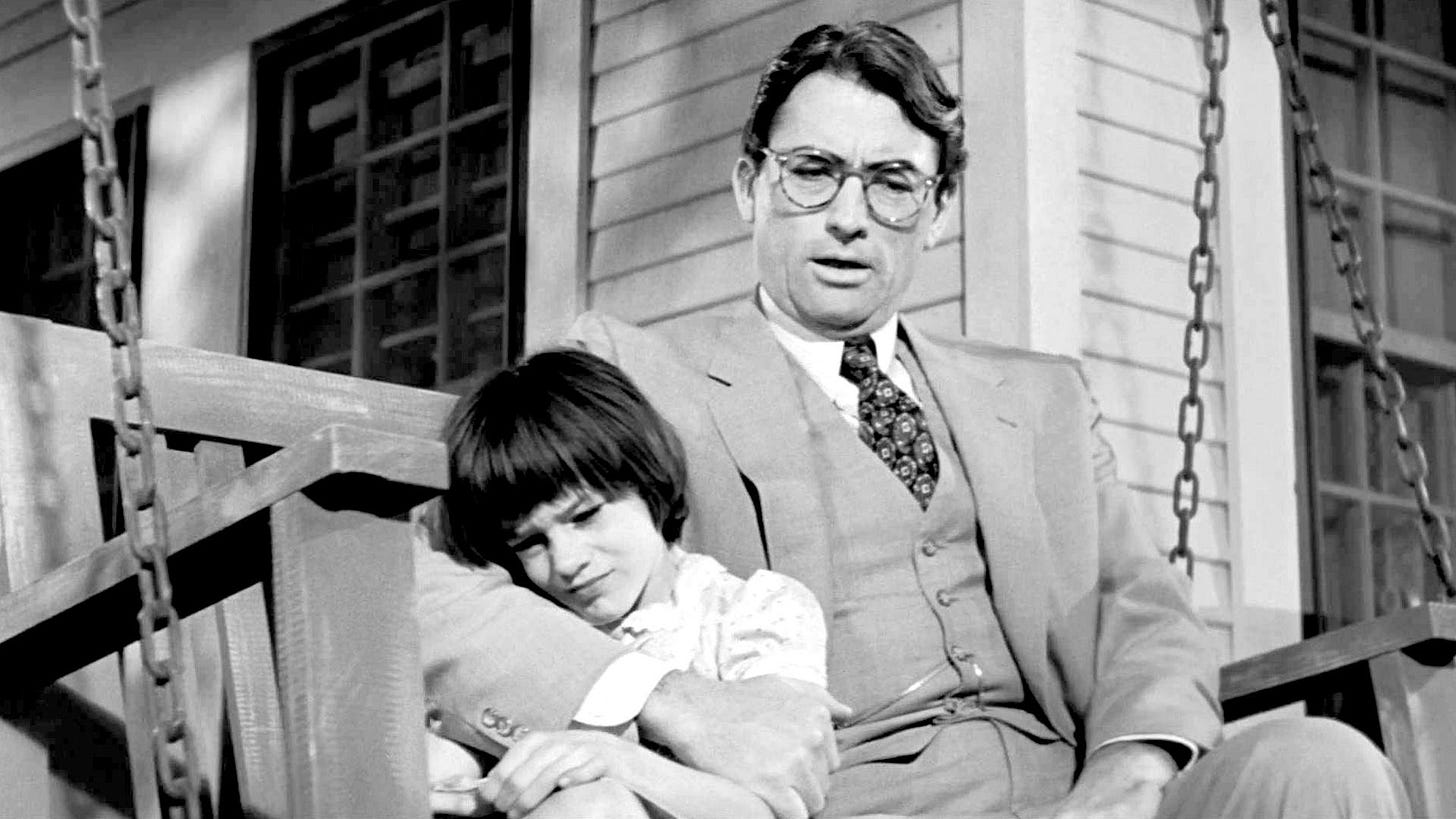 Gregory Peck and and an upset Mary Badham on a porch swing from the film To Kill a Mockingbird.