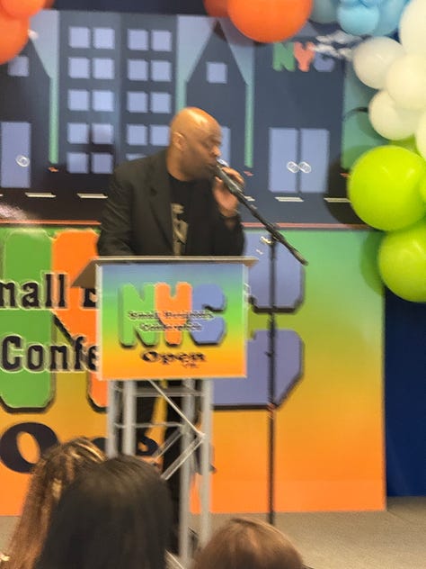 Left to Right: a man at a microphone, two women and a man at table that says nyc public schools, open for business, a man at a microphone on a podium