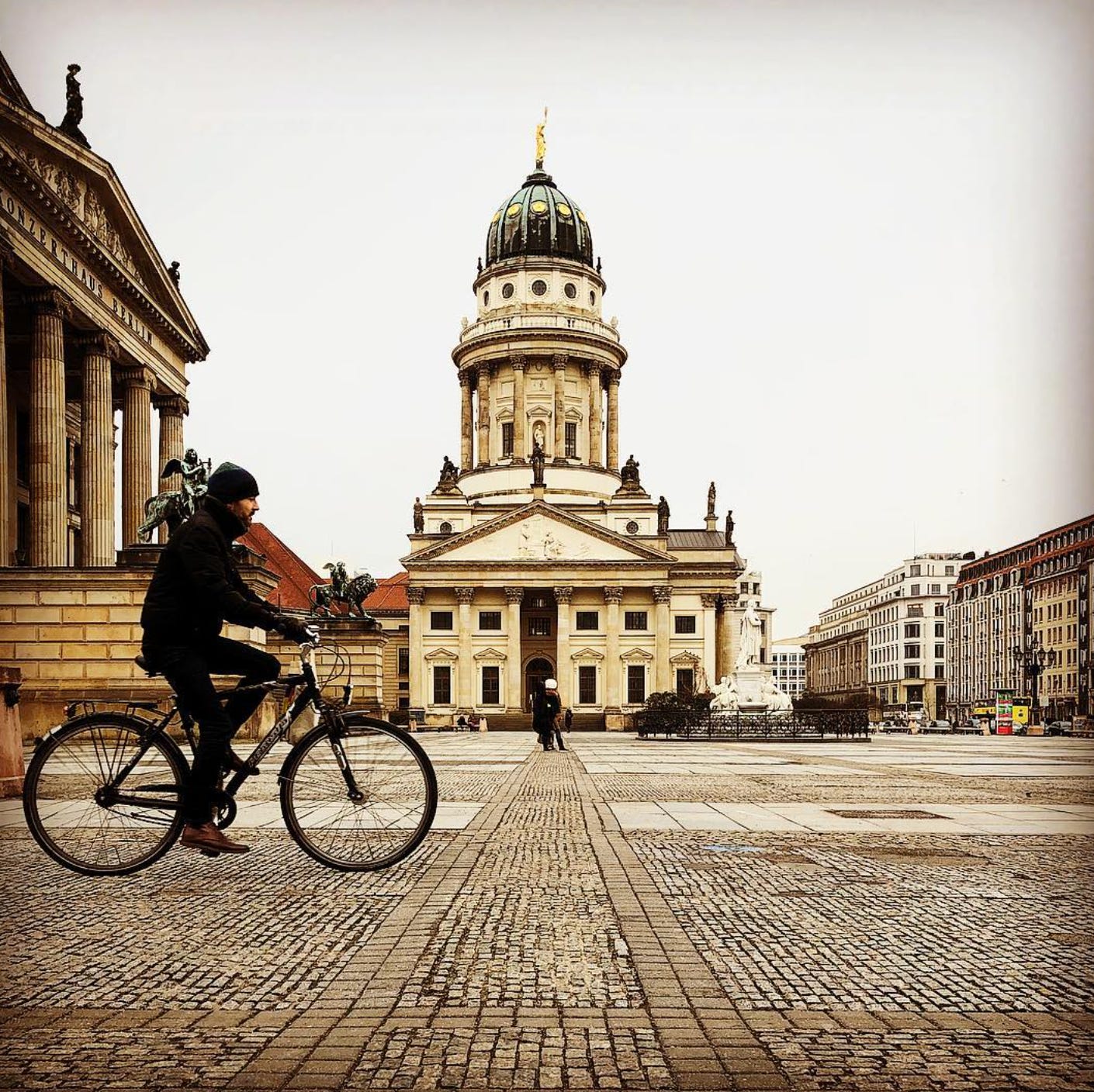 Cyclist riding across a cobblestone square in Berlin’s Mitte district, with the domed Französischer Dom (French Cathedral) in the background.